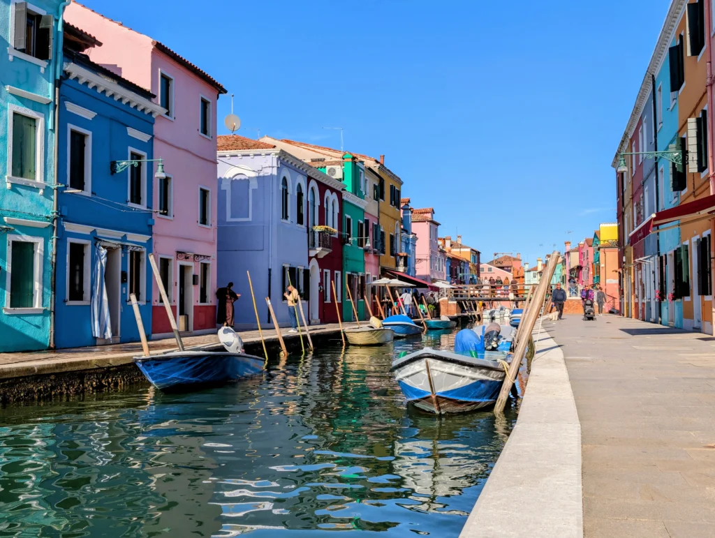 Kanal auf Burano mit bunten Fassaden und kleinen Booten unter blauem Himmel