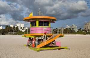 Miami mit Kindern - Bunter Lifeguard Tower am Strand von Miami Beach in South Beach mit Sand, Palmen und Wolkenhimmel
