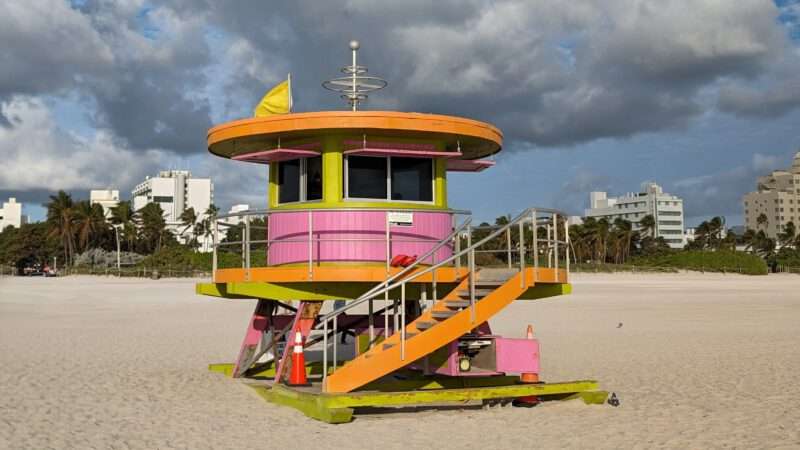 Miami mit Kindern - Bunter Lifeguard Tower am Strand von Miami Beach in South Beach mit Sand, Palmen und Wolkenhimmel