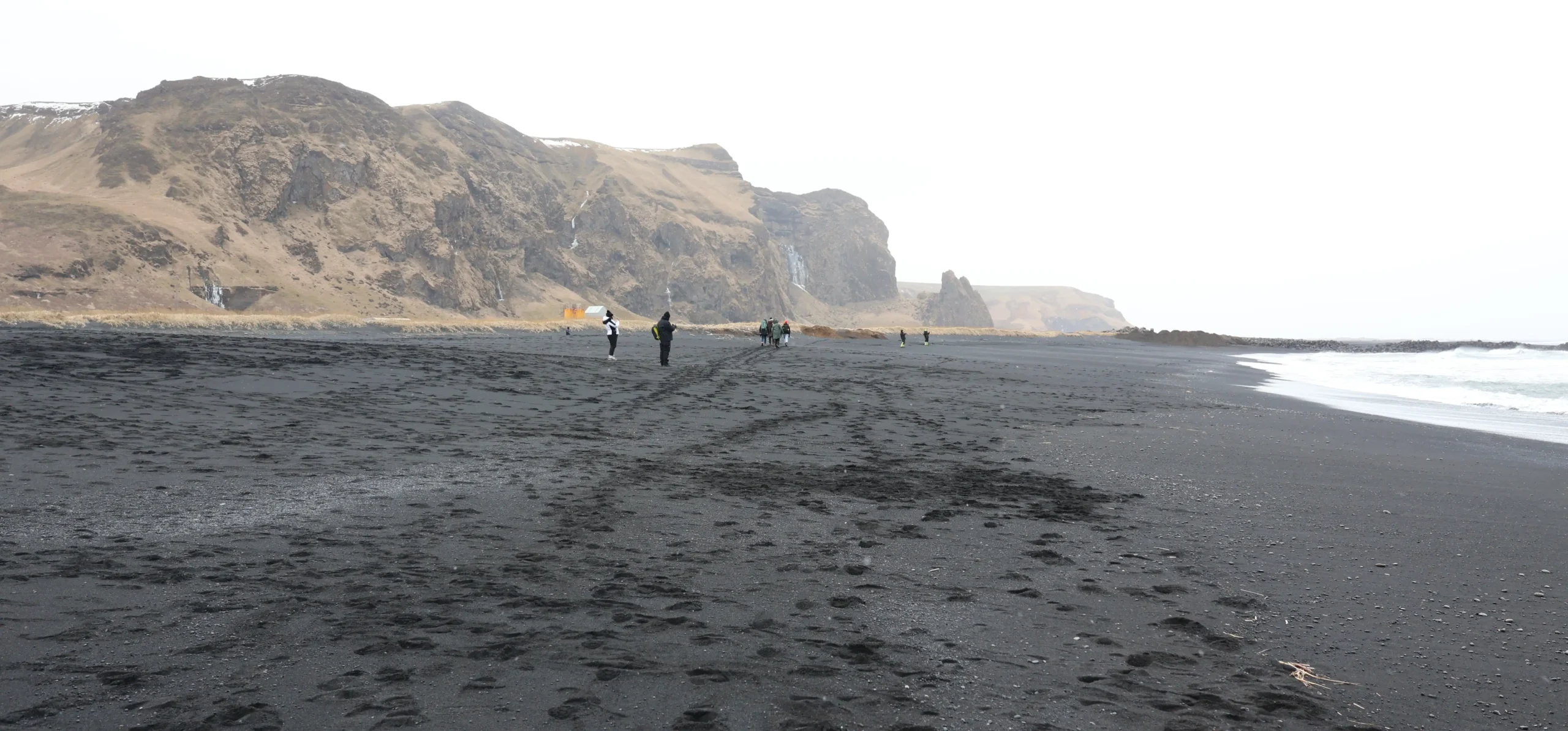 Brandung am schwarzen Strand von Reynisfjara mit Felsen im Hintergrund